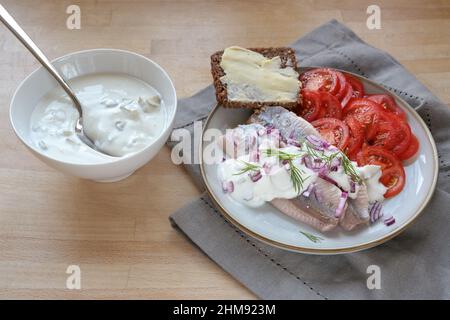 Filets de hareng salés avec tranches de tomate et pain complet brun sur une assiette et sauce à la crème aigre dans un bol, une serviette et une table en bois Banque D'Images