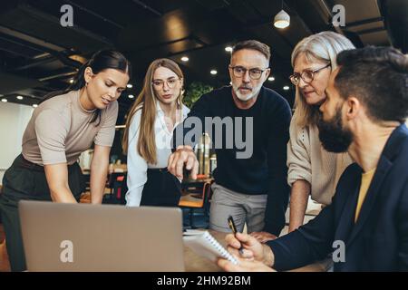 Personnes d'affaires ciblées ayant une discussion tout en collaborant à un nouveau projet dans un bureau. Groupe d'hommes d'affaires divers utilisant un ordinateur portable pendant que wor Banque D'Images