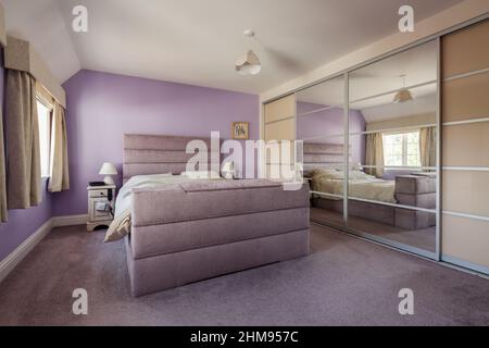 Burrugueux Green, Suffolk - juillet 12 2018: Lilas et blanc chambre décorée avec moquette et lit assortis et grande armoire à un mur avec miroir sl Banque D'Images