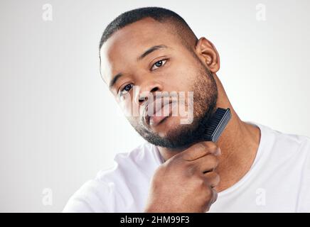 Le soin des cheveux du visage est un art délicat. Studio portrait d'un jeune homme beau brossant ses cheveux du visage sur un fond blanc. Banque D'Images