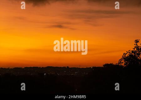 Coucher de soleil avec le ciel dans les couleurs orange et rose, avec quelques nuages, sur le côté gauche de sa base la ville s'allume en arrière-plan et sur le côté le si Banque D'Images