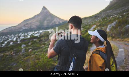 Cette vue est tout simplement époustouflante. Photo d'un jeune couple en train de prendre des photos lors d'une randonnée dans une chaîne de montagnes à l'extérieur. Banque D'Images