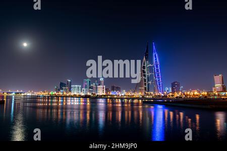 Une pleine lune brille au-dessus de la ligne d'horizon de Manama, Bahreïn, tandis que les lumières du World Trade Center et des bâtiments environnants se reflètent au large de la mer. Banque D'Images