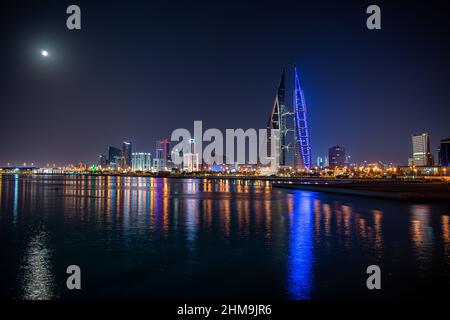 Une pleine lune brille au-dessus de la ligne d'horizon de Manama, Bahreïn, tandis que les lumières du World Trade Center et des bâtiments environnants se reflètent au large de la mer. Banque D'Images