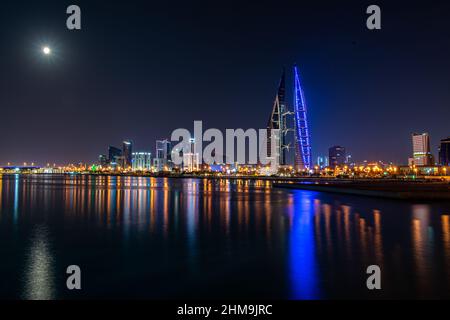 Une pleine lune brille au-dessus de la ligne d'horizon de Manama, Bahreïn, tandis que les lumières du World Trade Center et des bâtiments environnants se reflètent au large de la mer. Banque D'Images
