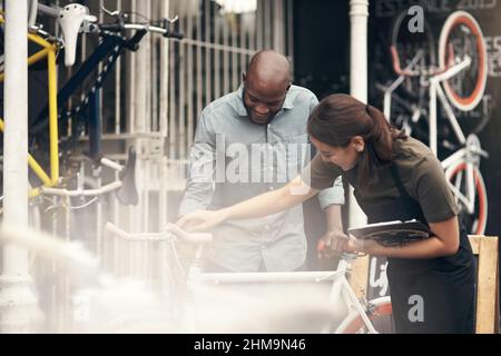 Pensez-vous que la coque comme ceci. Photo d'une jeune femme attirante se tenant à l'extérieur de son magasin de vélos et aidant un client. Banque D'Images