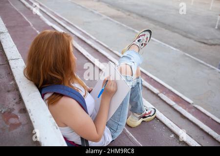adolescente dessine dans le carnet d'esquisses tout en étant assis sur les marches. Banque D'Images