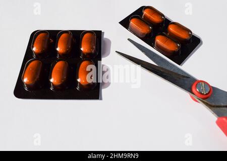 Bandelettes de médicaments de 10 comprimés en paquet de couleur marron coupées avec des ciseaux sur fond blanc Banque D'Images