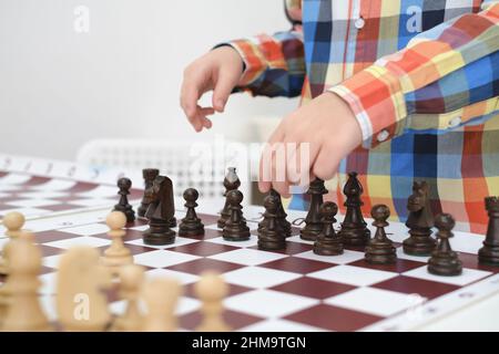 Gros plan main caucasien garçon jouant aux échecs. Heureux enfant concentré derrière les échecs dans la classe ou la leçon d'école. Excitée et astucieuse enfant de l'école élémentaire Banque D'Images