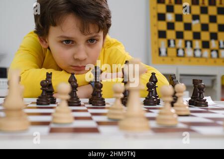 Un garçon caucasien jouant aux échecs. Heureux enfant concentré derrière les échecs dans la classe ou la leçon d'école. Un jeune enfant très intelligent de l'école élémentaire avec un jeu de société Banque D'Images