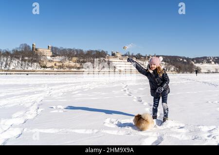Petite fille en vêtements chauds d'entraînement et de parler avec l'animal de compagnie de chien Spitz sur la neige Banque D'Images