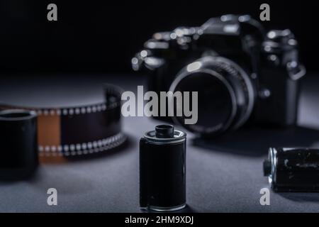 Photographie de film - une cartouche de film métallique vintage et un appareil photo reflex 35mm sur fond sombre. Banque D'Images