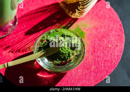 Thé matcha sain et poudre séchée près de chasen en bois et de Chashaku sur support rond lumineux sur table noire au soleil Banque D'Images