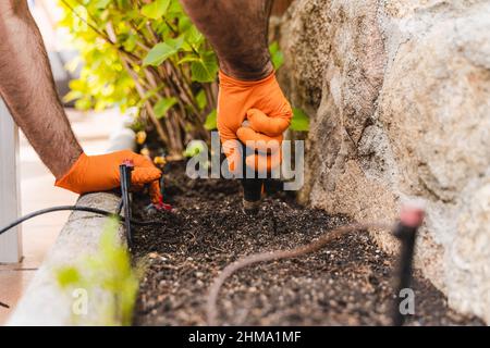 Cultivez un jardinier mâle méconnaissable dans un gant de latex en desserrant le sol fertile avec une fourche à main près du mur en pierre tout en travaillant dans le jardin Banque D'Images