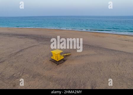 Vue aérienne spectaculaire de la tour des sauveteurs jaune vif située sur une rive sablonneuse en face de la mer bleue sous le ciel ensoleillé Banque D'Images