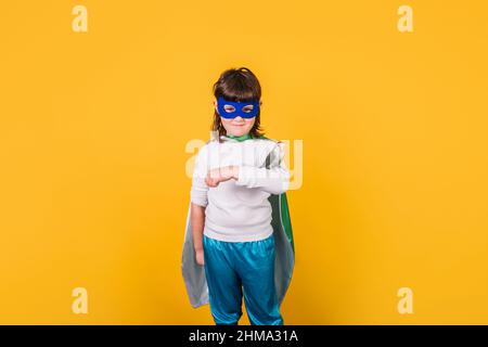 Charmante fille habillée comme super-héros regardant l'appareil photo sur fond jaune en studio et tenant perroquet sur le bras Banque D'Images