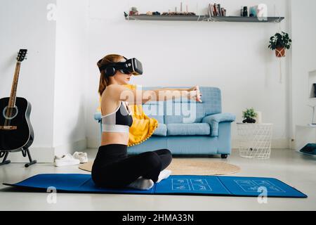 Vue latérale sur toute la longueur d'une femme anonyme en vêtements de sport s'étendant sur un tapis et se portant sur des jambes croisées lors de l'entraînement dans des lunettes VR à la maison Banque D'Images