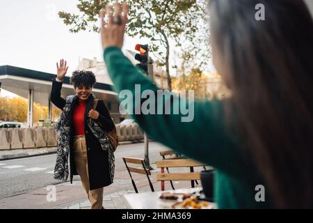 Une femme hispanique fait la main à un ami afro-américain enthousiaste tout en s'asseyant à table avec des desserts dans un café de rue Banque D'Images