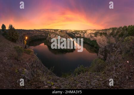 Lac calme entouré de rivage pierreux avec des plantes vertes contre le ciel coloré à l'heure du coucher du soleil dans la nature le soir d'été Banque D'Images