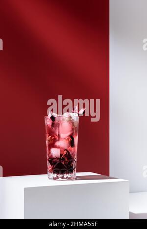 Composition de verre rempli de gin tonique rose et de glace placée sur une table blanche sur fond rouge Banque D'Images