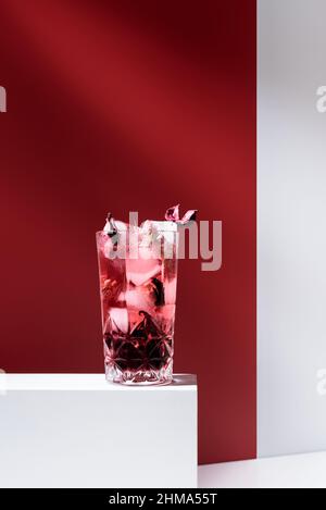 Composition de verre rempli de gin tonique rose et de glace placée sur une table blanche sur fond rouge Banque D'Images