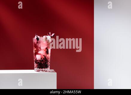 Composition de verre rempli de gin tonique rose et de glace placée sur une table blanche sur fond rouge Banque D'Images