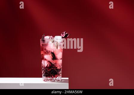 Composition de verre rempli de gin tonique rose et de glace placée sur une table blanche sur fond rouge Banque D'Images