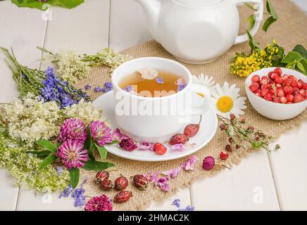 Tisane au rosehip, camomille et trèfle dans une tasse blanche sur une table blanche en bois avec des fleurs. Banque D'Images