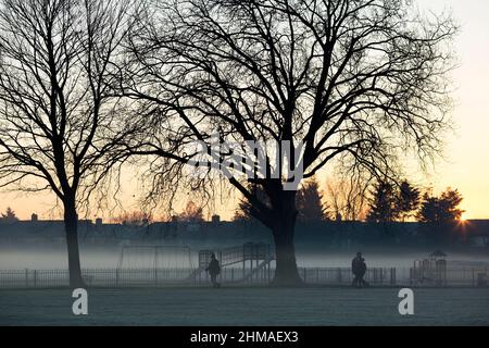Les gens marchent dans un parc couvert de brume et de gel à Ilford, dans l'est de Londres, au lever du soleil. Banque D'Images