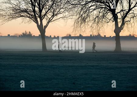 Les gens marchent dans un parc couvert de brume et de gel à Ilford, dans l'est de Londres, au lever du soleil. Banque D'Images