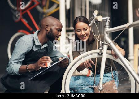 C'est ici qu'il s'agit. Photo d'un beau jeune homme qui s'est accroupi devant son magasin de vélos et a aidé un client. Banque D'Images