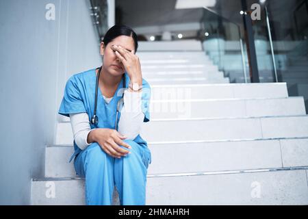 Parfois, tout n'est pas entre nos mains. Photo d'une infirmière qui regarde stressée tout en étant assise sur un escalier. Banque D'Images