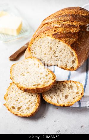 Pain de levain tranché artisanal fait maison sur une serviette et beurre avec couteau. Concept de cuisson maison saine. Banque D'Images