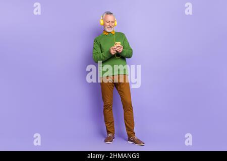 Photo de joli mignon retraité homme porter un chandail vert appréciant des chansons moderne appareil isolé couleur violet fond Banque D'Images