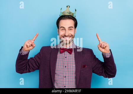 Photo de jeune homme joyeux et charmant indiquer les doigts Golden Crown marque isolée sur fond bleu de couleur Banque D'Images