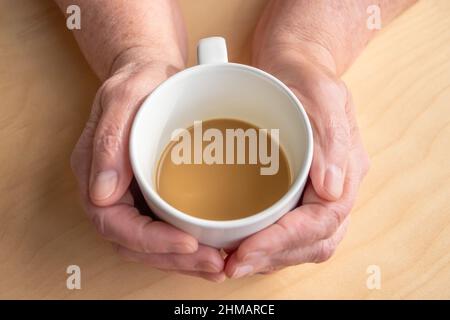 Une femme âgée tient le café du matin avec du lait dans les mains, sur une table en bois Banque D'Images