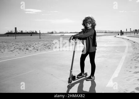 Enfant en scooter dans le parc. Super héros enfant dans un manteau rouge super-héros. Super héros concept. Banque D'Images