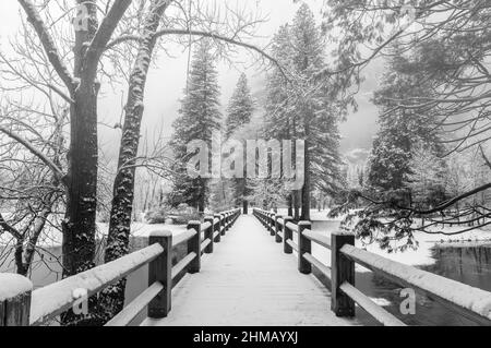 Une nouvelle neige fraîche couvre le pont au-dessus de la rivière Merced après une tempête d'hiver dans le parc national de Yosemite, Californie, États-Unis. Banque D'Images