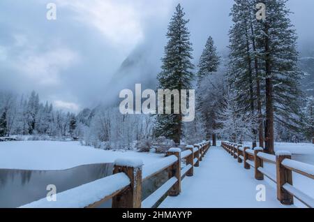 Une nouvelle neige fraîche couvre le pont au-dessus de la rivière Merced après une tempête d'hiver dans le parc national de Yosemite, Californie, États-Unis. Banque D'Images