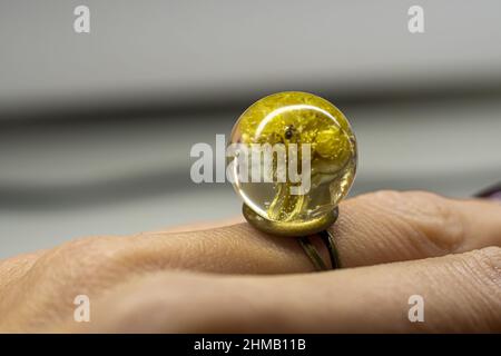 Gros plan d'un anneau en résine époxy sur le doigt d'une femelle - fleurs jaunes séchées dans un morceau de bijoux Banque D'Images