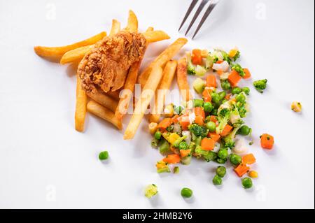 Un morceau de viande de poulet frite en flocons de maïs, frites et légumes ( pois, carottes, maïs, chou-fleur et brocoli) éparpillés sur fond blanc, p Banque D'Images