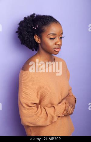 Une jolie jeune femme britannique noire se tenant sur un fond violet et regardant loin Banque D'Images