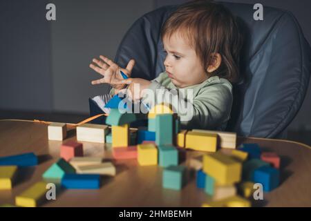 Bébé fille jouant avec des cubes de jouet de connexion à la maison. Éducation des enfants. Jouets en bois. Jeux pour enfants. Bureau en bois, table. Banque D'Images