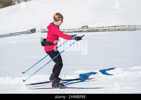 Une femme d'âge moyen, une skieuse sportive de fond, fait du ski sur la piste de ski vide de la montagne. Banque D'Images