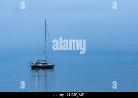 Le voilier noir est seul, se reflétant dans la mer calme pendant l'heure bleue, Danemark, 30 août 2017 Banque D'Images