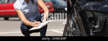 Une femme inspecteur écrit dans des documents sur le presse-papiers près d'une voiture brisée.Assurance automobile Banque D'Images