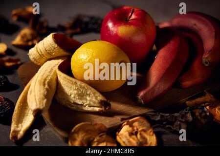 Planche à fruits. Bananes, citron, pomme et fruits secs en tranches sur un panneau de bois avec un fond sombre et flou. Banque D'Images