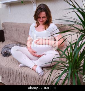 La femme enceinte tient son ventre à l'intérieur de la maison, le mode de vie Banque D'Images