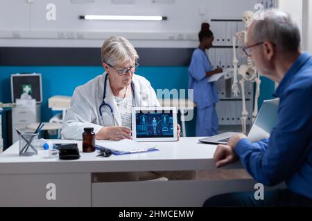 Medic montrant le comprimé avec l'illustration de l'analyse du corps humain à l'homme âgé. Un spécialiste de la santé explique le diagnostic au patient malade tout en tenant l'appareil avec une anatomie virtuelle et une expertise Banque D'Images