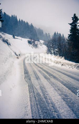 Route enneigée et glacée le long d'une pente en mauvais temps. Banque D'Images